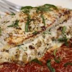 side view of three-cheese stuffed chicken with sausage and red sauce topped with fresh parmesan and basil