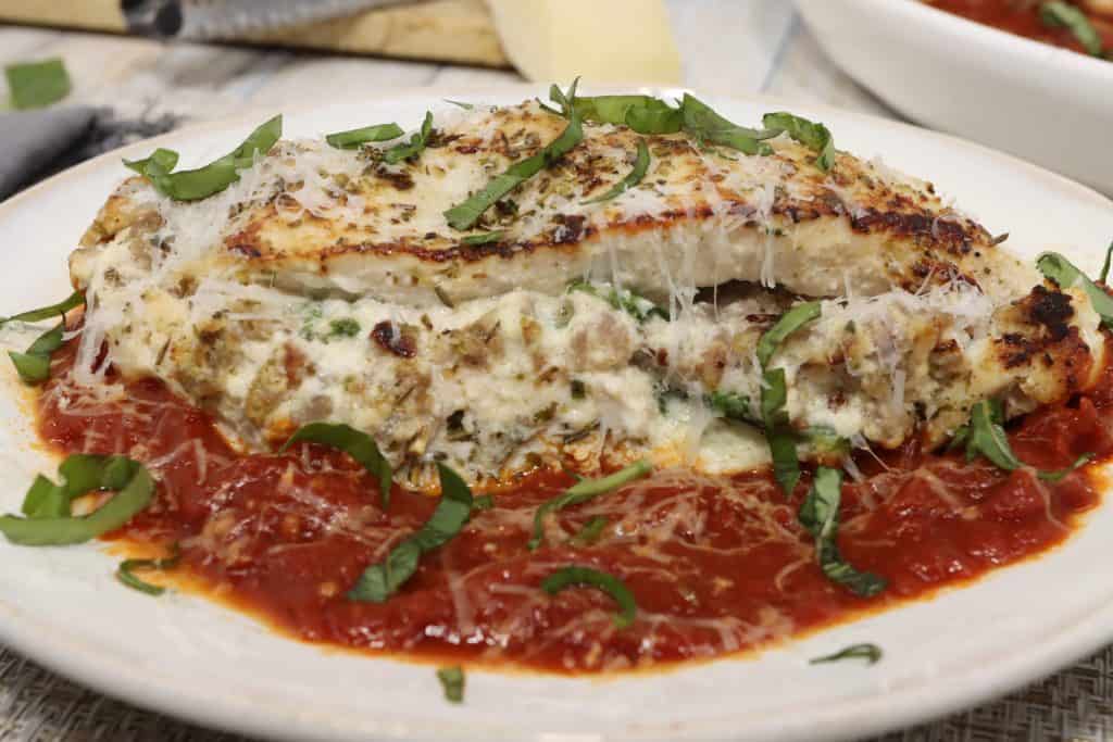 Plate with three-cheese stuffed chicken with sausage and red sauce topped with fresh parmesan and basil