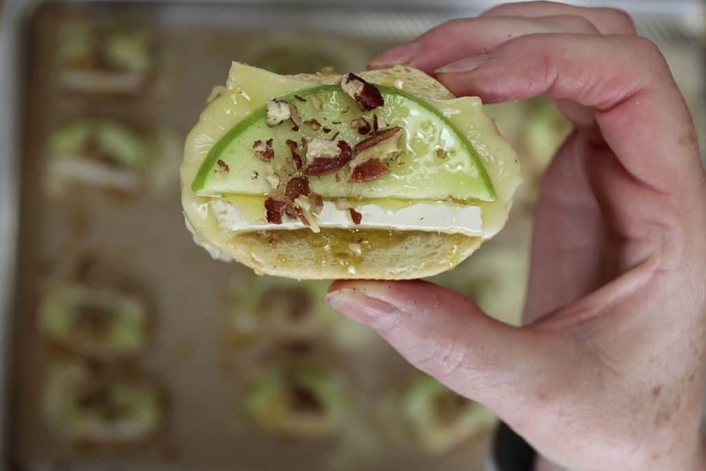 holding one crostini with melted brie apple pecans and honey