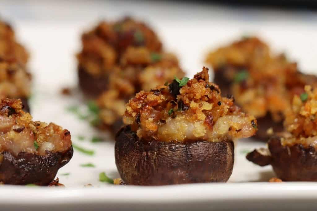 close up of stuffed mushroom with sausage and bread crumbs on a platter