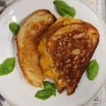 bbq chicken panini with cheddar and basil cut in half on a plate with basil leaves
