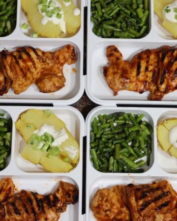 overhead view of healthy meal prep idea: bento boxes with easy meal prep - four bento boxes with close up look at one bento box with Grilled BBQ chicken thighs with potato & asparagus