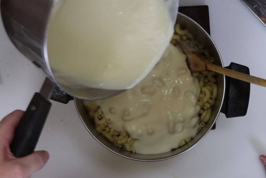 pouring the cheddar, gruyere, goat cheese sauce over elbow macaroni