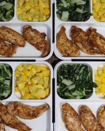overhead view of four meal prep containers with garam masala tenders with garlic bok choy and yellow squash