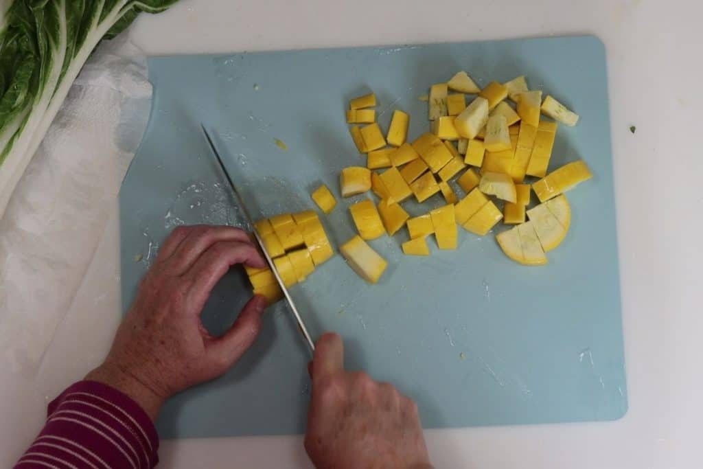 chopping yellow summer squash into cubes for garam masala meal prep chicken tenders