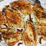 overview picture of a platter of stuffed chicken with sundried tomatoes and cheese garnished with feta parsley