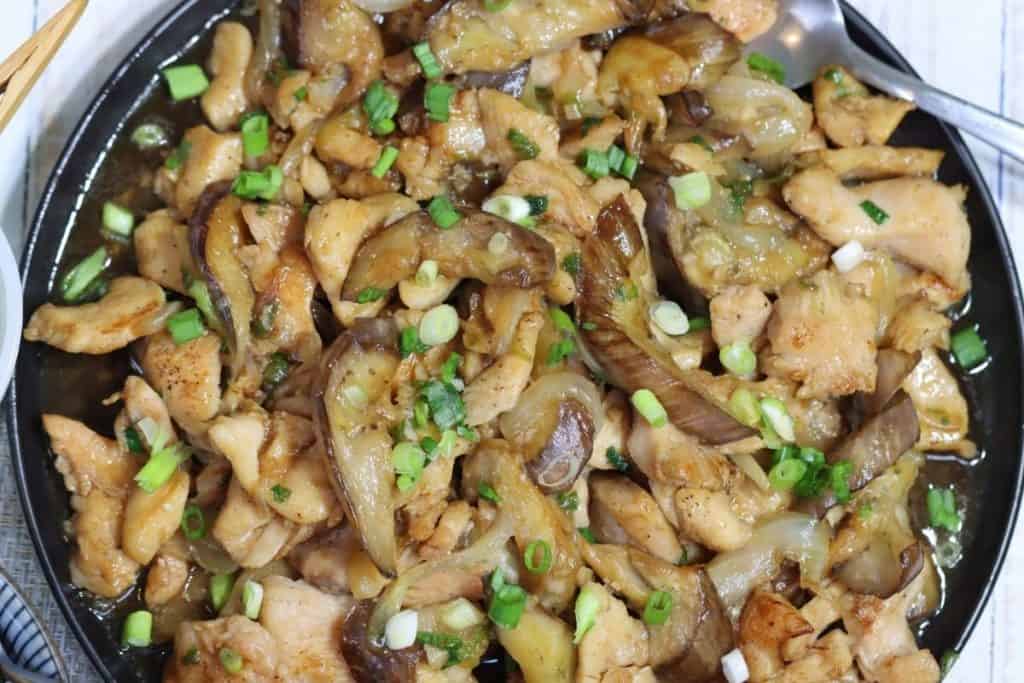 overhead view of a serving plate filled with asian style chicken & eggplant stir fry topped with scallions