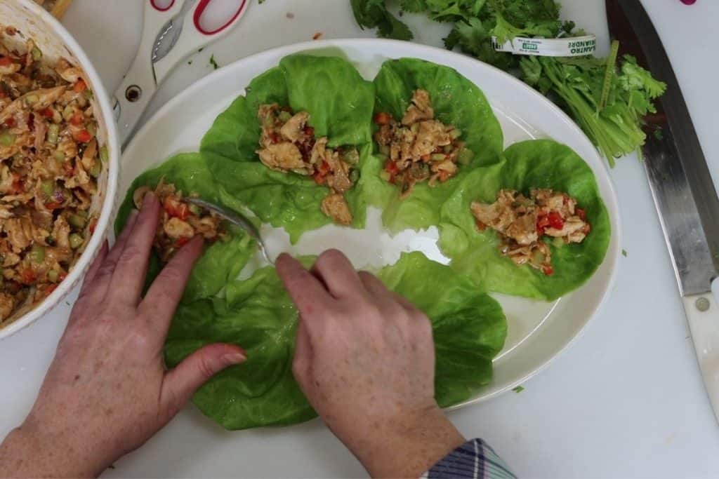 assembling the thai lettuce wraps with rotisserie chicken on a platter