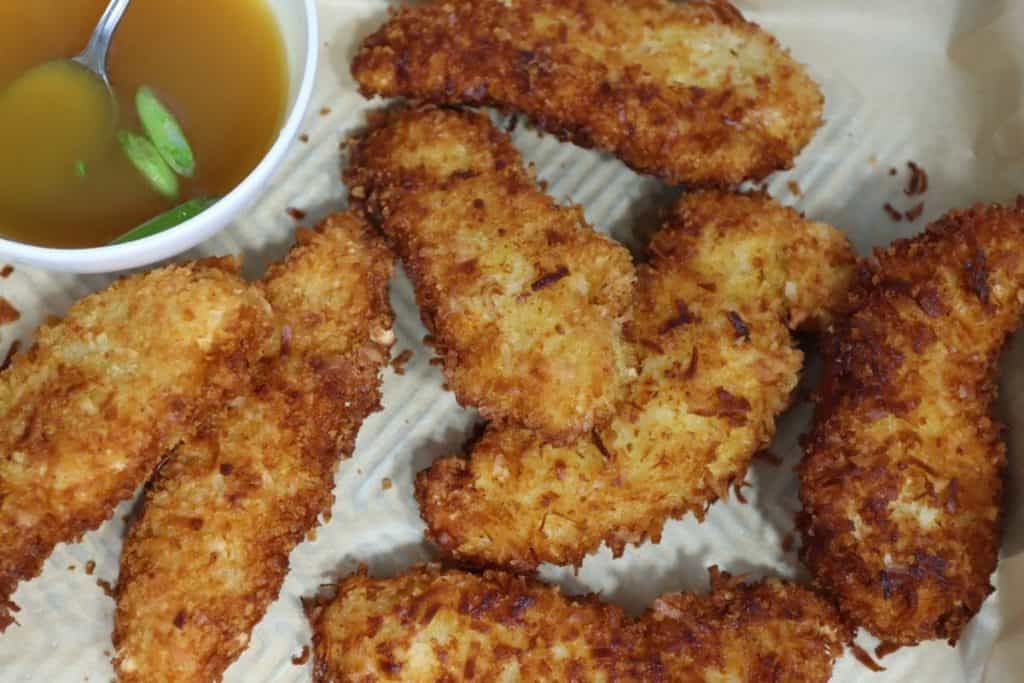 close up of crunchy coconut chicken fingers on a sheet pan with homemade honey mustard sauce