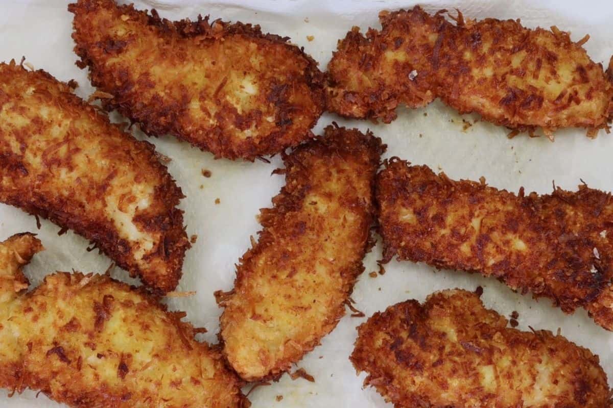 crunchy coconut chicken fingers on paper towel lined sheet pan
