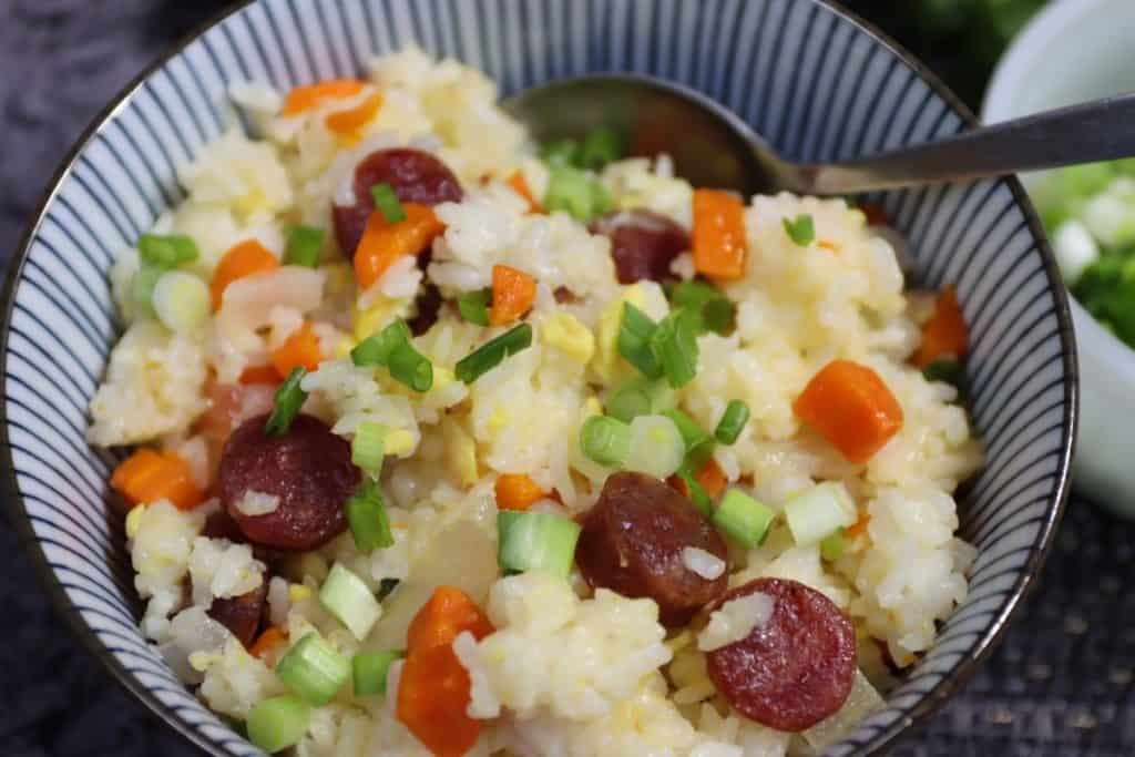 close up of a single portion of fried rice with chinese sausage in blue striped bowl