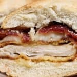 close up look of kackle burger chicken cutlet with bacon and cheese on french bread cut in half