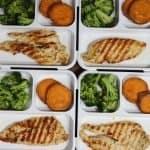 overhead view of four bento boxes on a table with grilled rosemary chicken broccoli and sweet potatoes