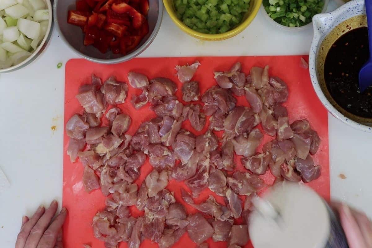 overhead view of the prep: all the diced veggies, sweet and spicy sauce, seasoning the chicken on the cutting board