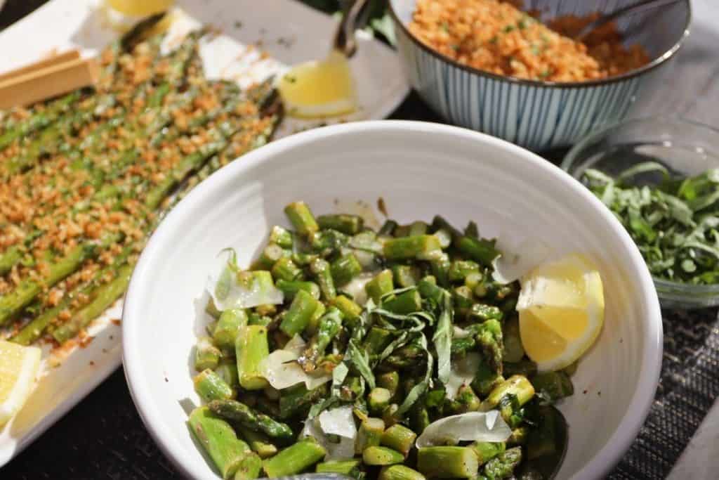 bowl of sauteed spring asparagus with basil and shaved parmesan with platter of asparagus in the background