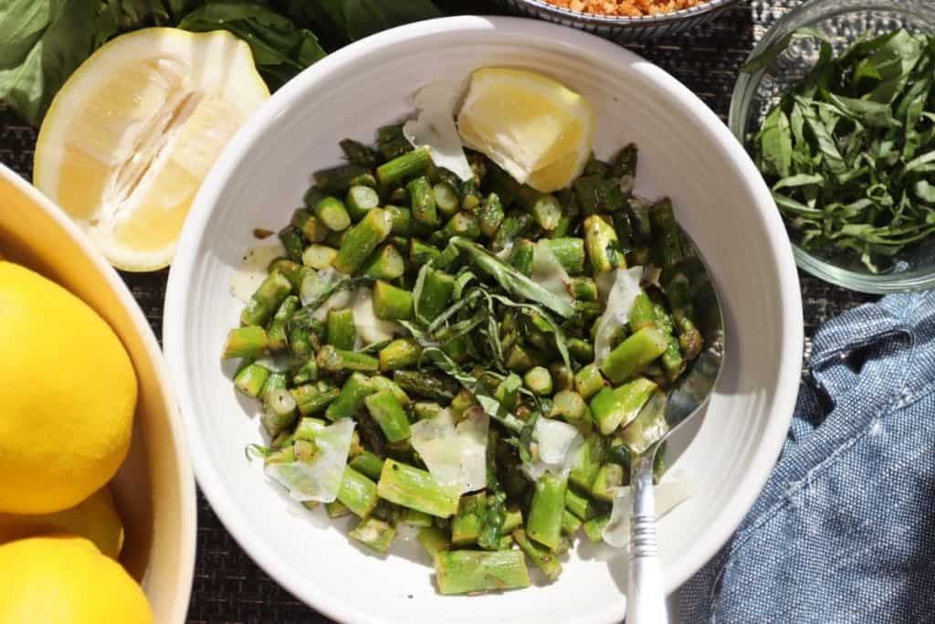 serving bowl of sauteed spring asparagus with fresh basil and shaved parmesan with lemon wedge