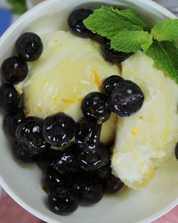 vanilla ice cream topped with blueberries, orange zest and honey mixture and garnished with mint leaves