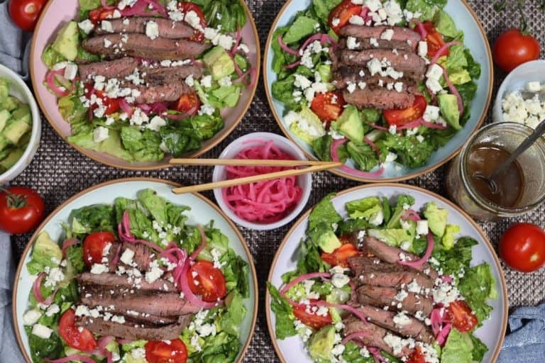 overhead shot of four steak salads with pickled red onions and bleu cheese as well as campari tomatoes, avocado chunks and homemade balsamic vinaigrette