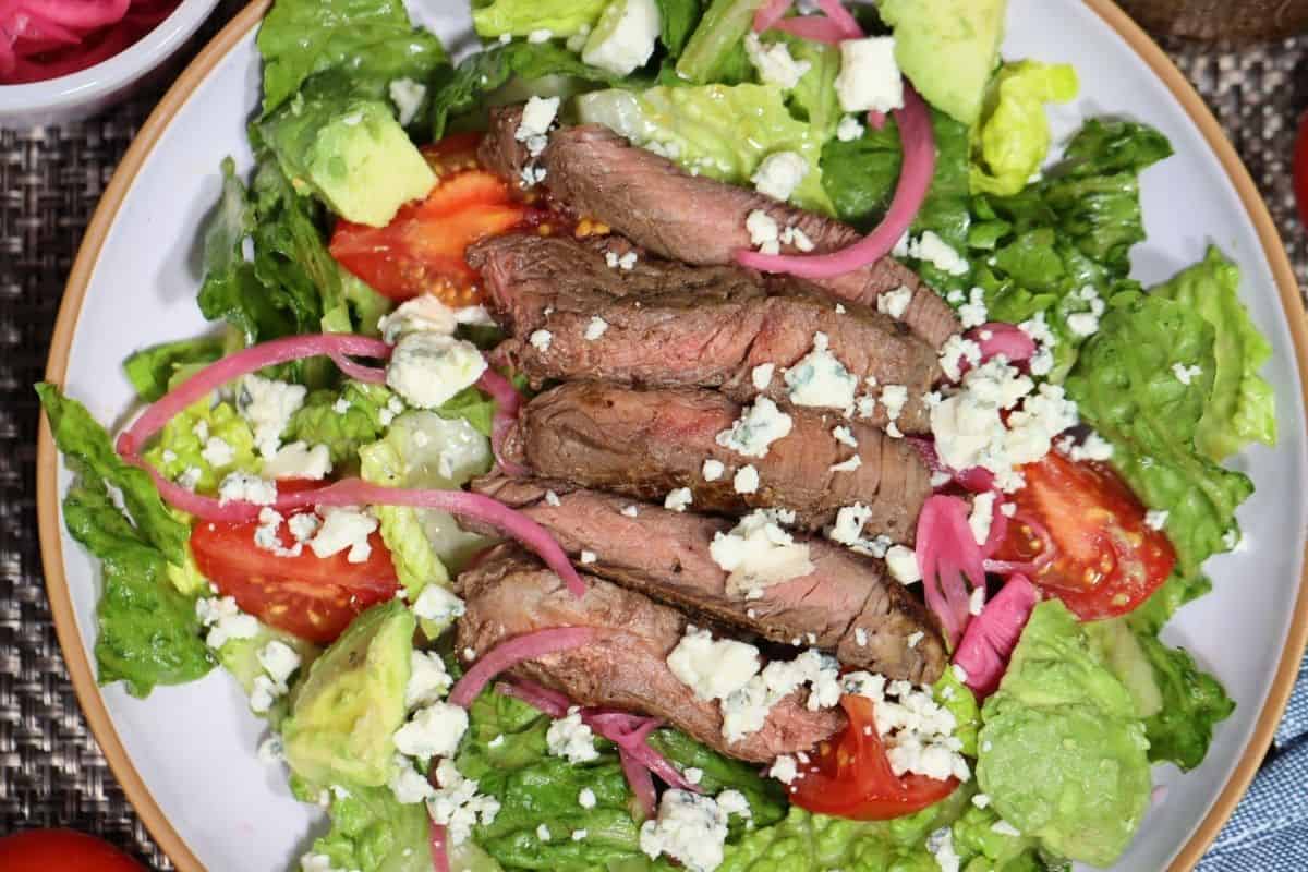 overhead shot of steak salad with pickled red onions and bleu cheese as well as campari tomatoes, avocado chunks and homemade balsamic vinaigrette