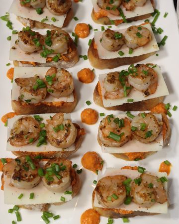 overhead view of garlic shrimp crostini with romesco sauce and shaved parmesan