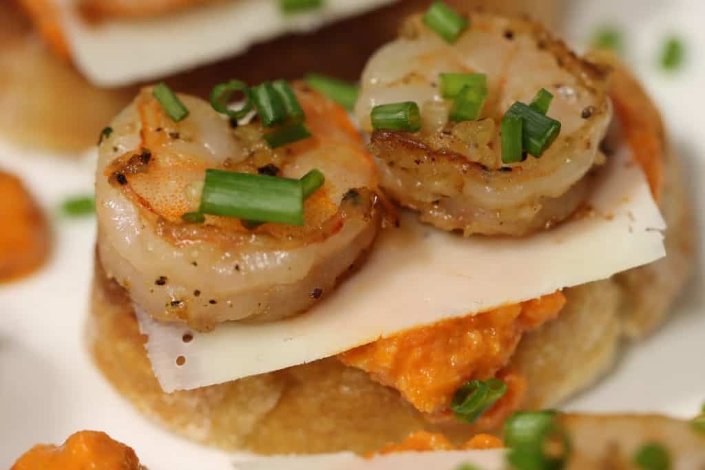 a closer look at one garlic shrimp crostini with romesco sauce and shaved parmesan and topped with fresh chives
