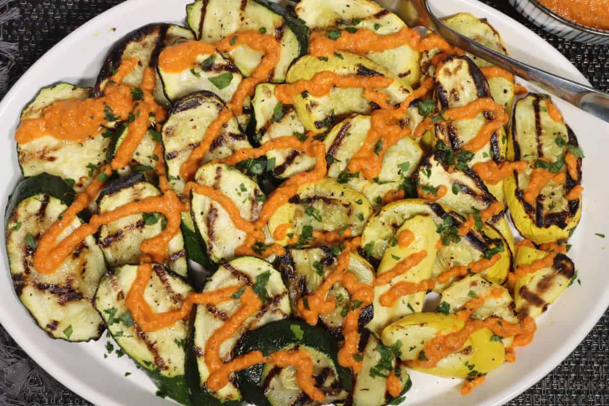 platter of grilled zucchini and summer squash with romesco sauce drizzled over the top