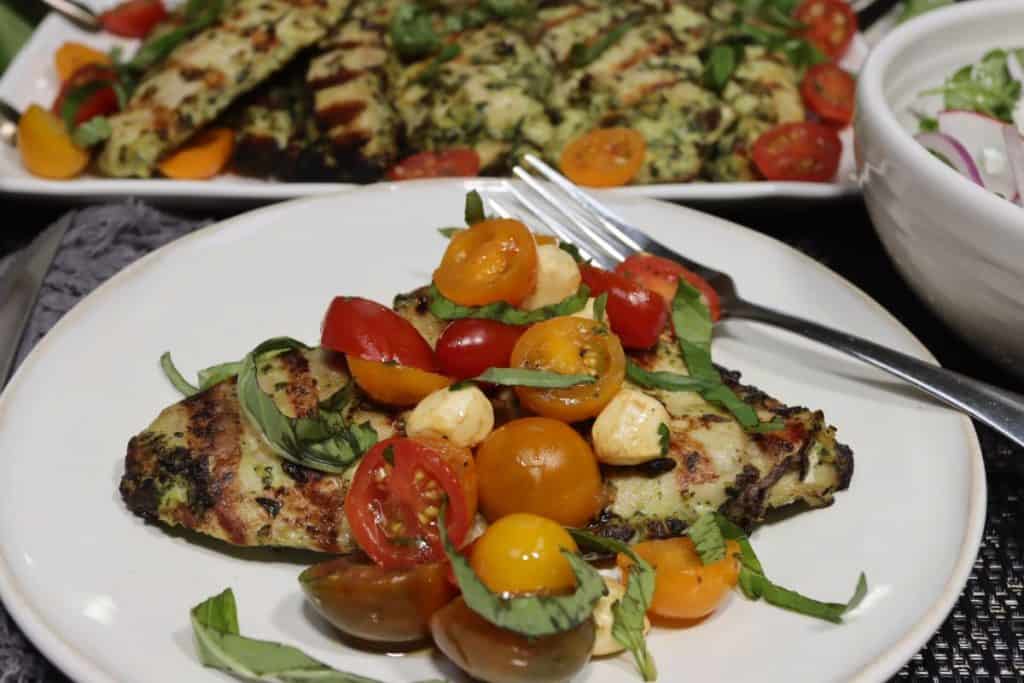 one plate of the best grilled chicken with marinated tomatoes with platter of chicken in background and arugula salad to the right