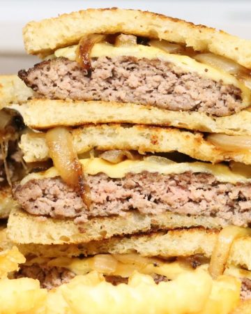 front view of a platter of crunchy cheesy patty melts with sauteed onions and crinkle fries