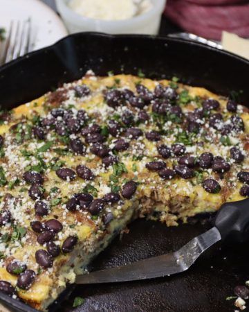 head-on view of pork carnitas skillet frittata topped with black beans, cotija cheese and cilantro with slice of frittata in background