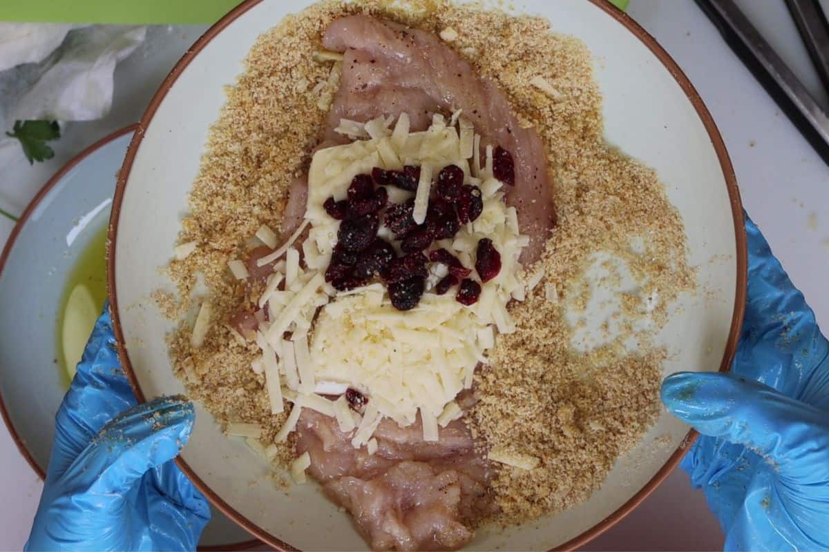during the assembly process the chicken is layed in breadcrumbs while slices of brie, sharp provolone cheese and craisins are placed on top before rolling
