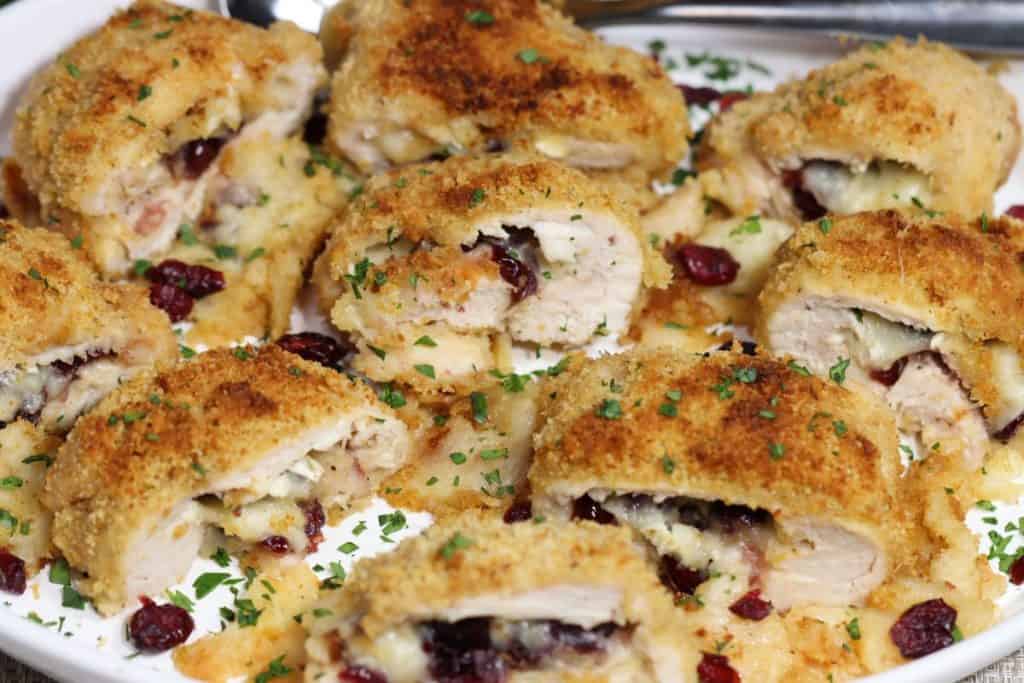 head on view of a platter of cranberry brie stuffed chicken garnished with fresh chopped parsley and craisins