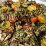 side view of grilled chimichurri chicken thighs with extra sauce spooned over the top and cherry tomatoes