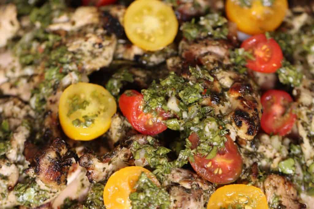 close up look of grilled chimichurri chicken thighs on a plate garnished with cherry tomatoes