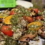 side view of a platter of grilled chimichurri chicken thighs with extra sauce and cherry tomatoes