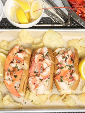 overhead view of simple buttery lobster rolls with butter, lemon, chives and chips. lobster shells in the background