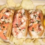 overhead shot of three mouth-watering lobster rolls garnished with fresh chives. serve with lemons and chips on the side
