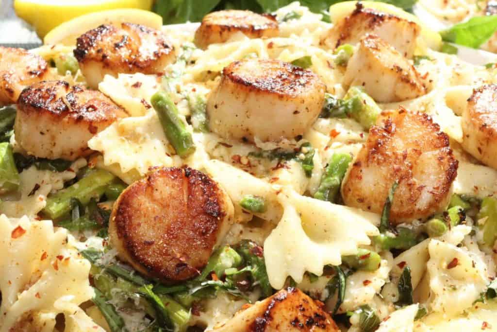very close look at pan seared sea scallops with basil brown butter, asparagus, farfalle, red pepper flakes and fresh parm on top