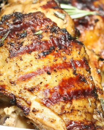 very close look a one rosemary balsamic grilled chicken thigh with asparagus in the background