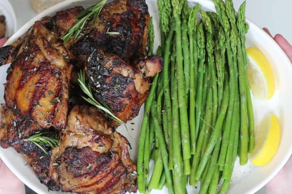 overhead view of a platter with rosemary balsamci grilled chicken thighs with steamed asparagus