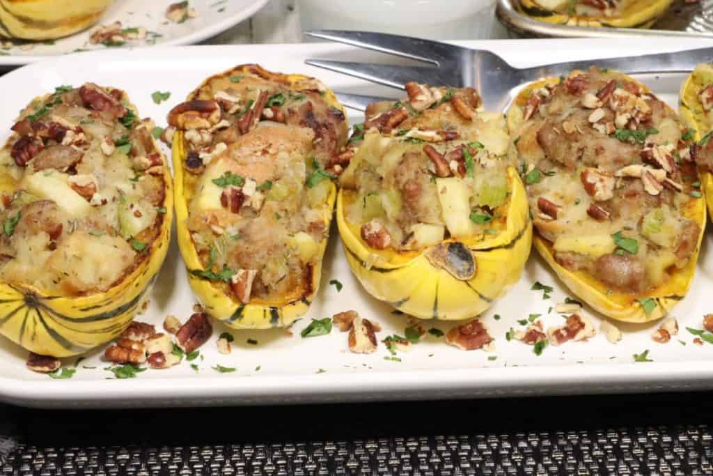 front view of platter of roasted delicata squash with sausage stuffing with pecan and parsley garnish