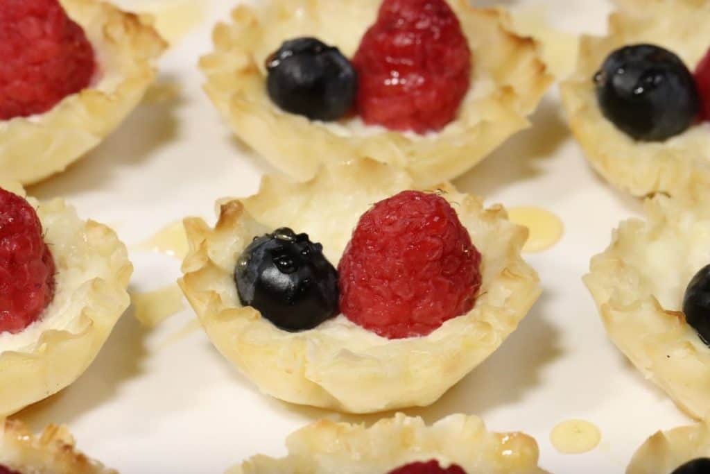 close up look at holiday appetizers phyllo cups five ways mascarpone raspberry blueberry bites on a serving tray with drizzled honey