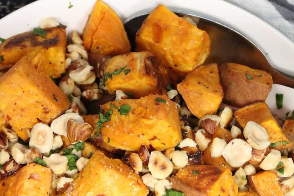 roasted sweet potatoes in a serving bowl topped with toasted hazelnuts and garnished with fresh parsley
