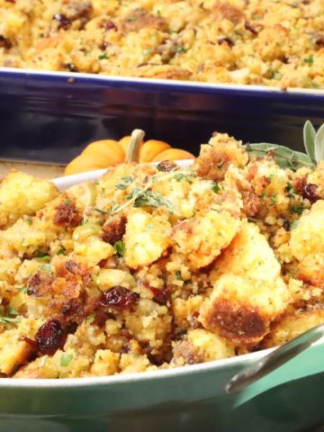 side view of a serving bowl of cornbread stuffing with sausage and the larger baking dish in the background. Table decorated with assorted ghourds