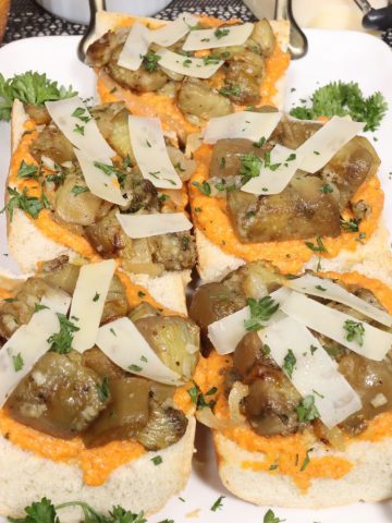close up front view of french bread pizza with romesco sauce and sauteed eggplant, shaved parmesan cheese and parlsey garnish on a small serving platter