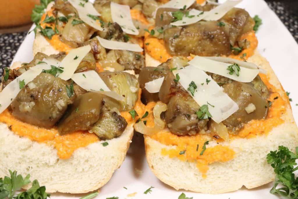 close up front view of french bread pizza with romesco sauce and sauteed eggplant, shaved parmesan cheese and parlsey garnish on a small serving platter