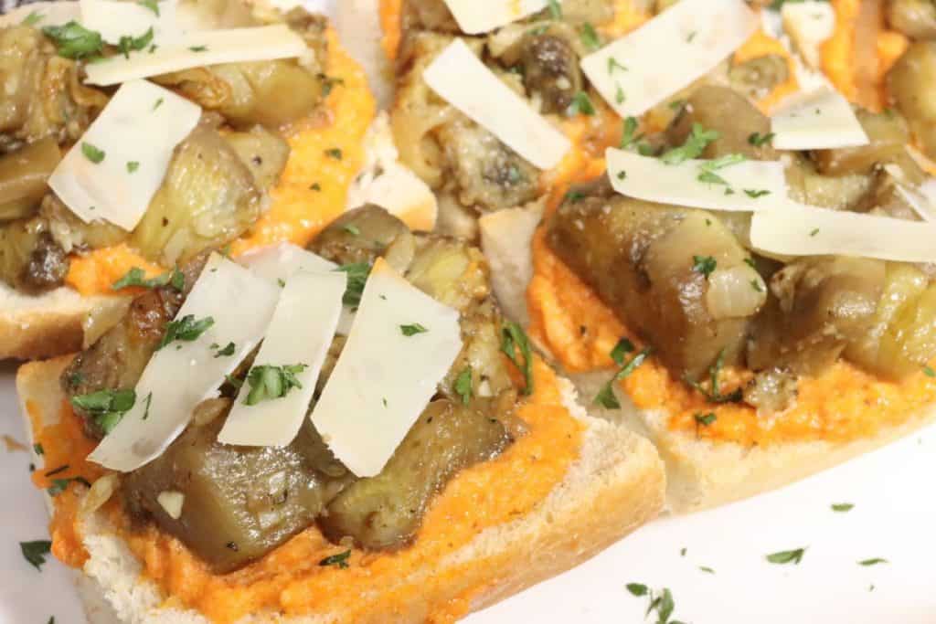 side view of french bread pizza with romesco sauce, sauteed eggplant and shaved parmesan cheese on a serving platter.