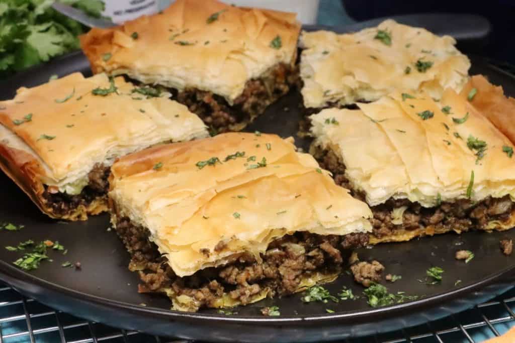 close up side view of moroccan-spiced phyllo meat pie on a serving plate garnished with cilantro