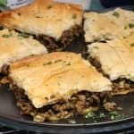 close up side view of moroccan-spiced phyllo meat pie on a serving plate garnished with cilantro