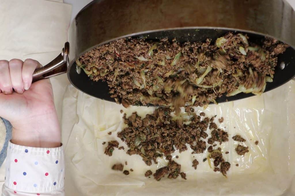 moroccan-spiced phyllo meat pie - transfer meat filling into phyllo dough lined baking dish