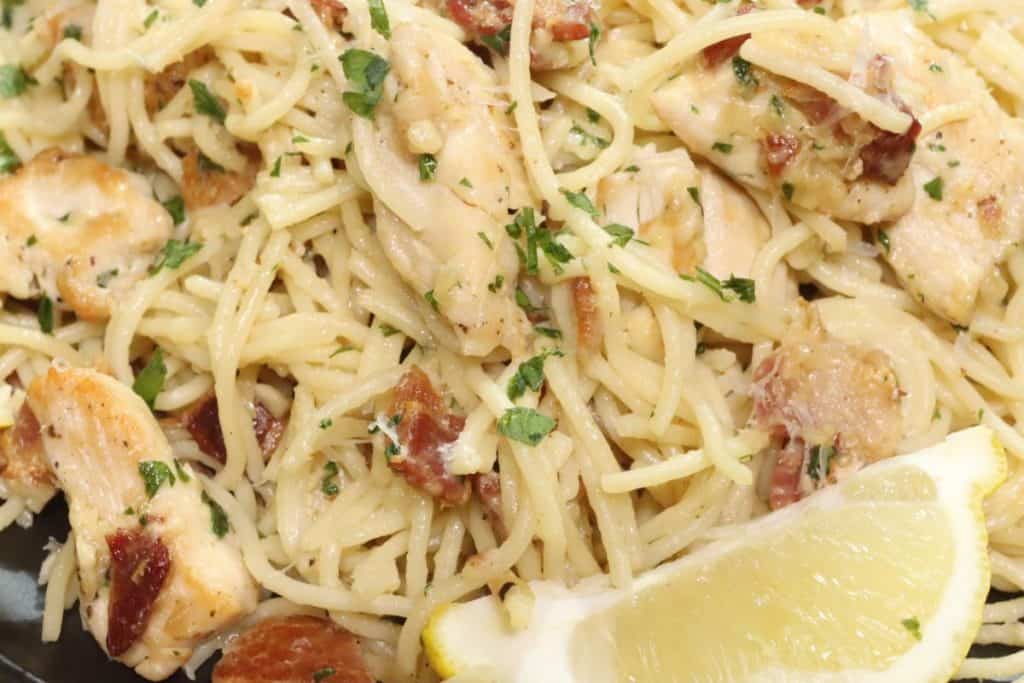 a very close look at a pile of creamy chicken bacon pasta with parsley and a lemon wedge